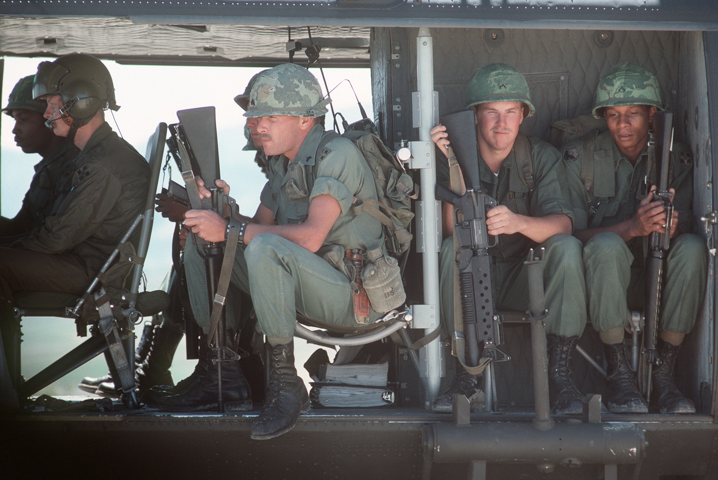 US Army soldiers ride on UH-1 Huey helicopter with M16A1 rifles