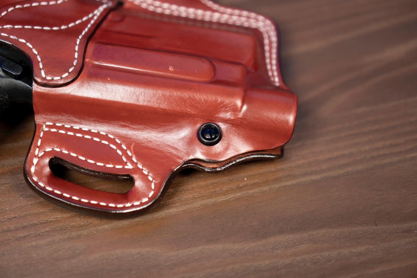 This image shows a close-up view of a pistol being secured into the DeSantis T.B. Vengeance holster, highlighting its superior American full-grain steer leather construction and precision stitching. The holster is designed to provide excellent firearm retention with its innovative thumb break mechanism and adjustable tensioning device. It offers a secure fit for handguns and pistols, making it ideal for both concealed carry and open carry applications. The detailed craftsmanship, including reinforced belt loops and triple stitching, ensures durability and functionality. The photo illustrates a key step in holstering, emphasizing the blend of quality design and practical application. Keywords such as holster, handgun, pistol, concealed carry, firearm, premium leather holster, and review desantis are integrated into this description. This comprehensive ALT text assists visually impaired users by providing an in-depth explanation of the holster's secure design and performance features.