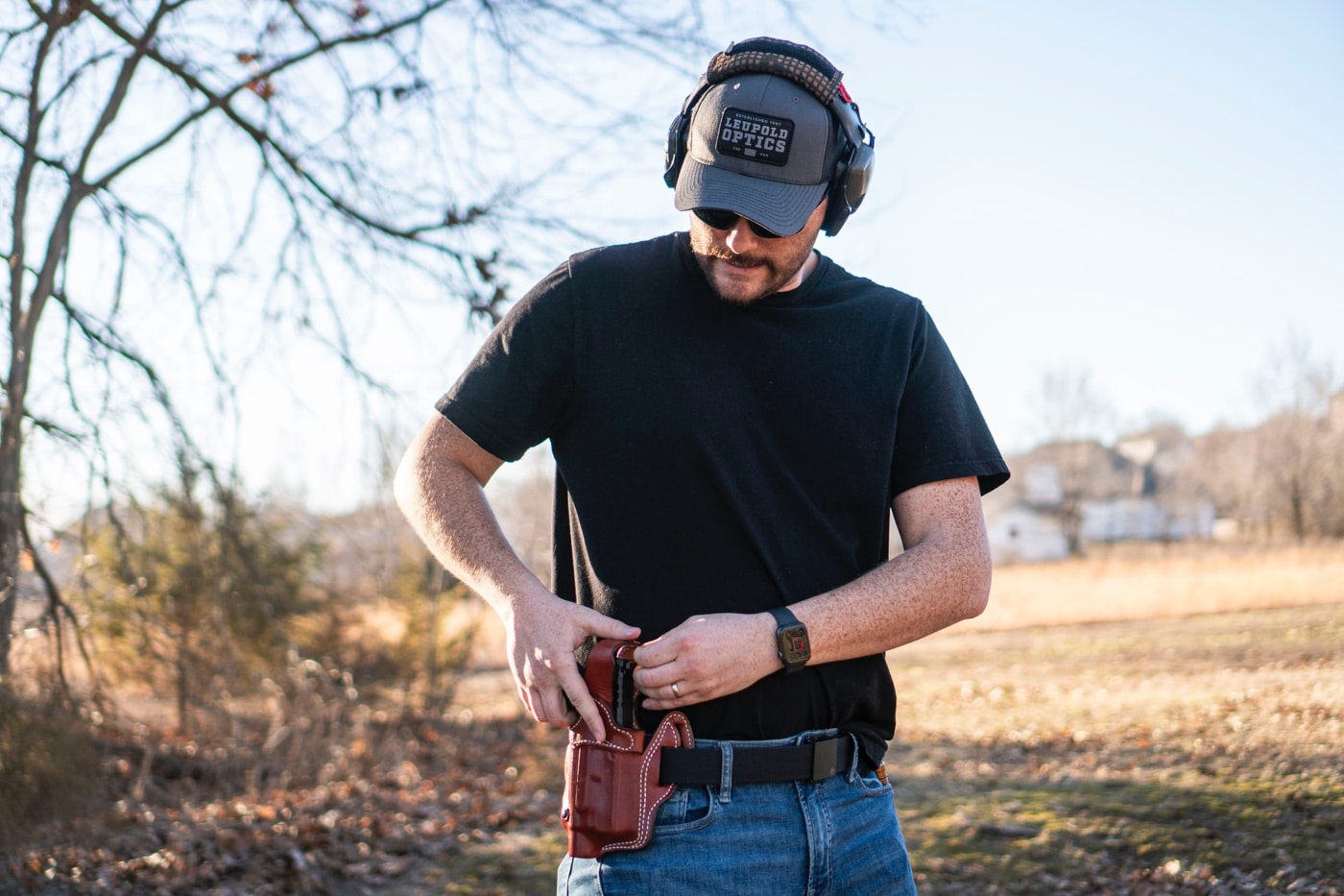 This image shows a close-up view of a pistol being secured into the DeSantis T.B. Vengeance holster, highlighting its superior American full-grain steer leather construction and precision stitching. The holster is designed to provide excellent firearm retention with its innovative thumb break mechanism and adjustable tensioning device. It offers a secure fit for handguns and pistols, making it ideal for both concealed carry and open carry applications. The detailed craftsmanship, including reinforced belt loops and triple stitching, ensures durability and functionality. The photo illustrates a key step in holstering, emphasizing the blend of quality design and practical application. Keywords such as holster, handgun, pistol, concealed carry, firearm, premium leather holster, and review desantis are integrated into this description. This comprehensive ALT text assists visually impaired users by providing an in-depth explanation of the holster's secure design and performance features.