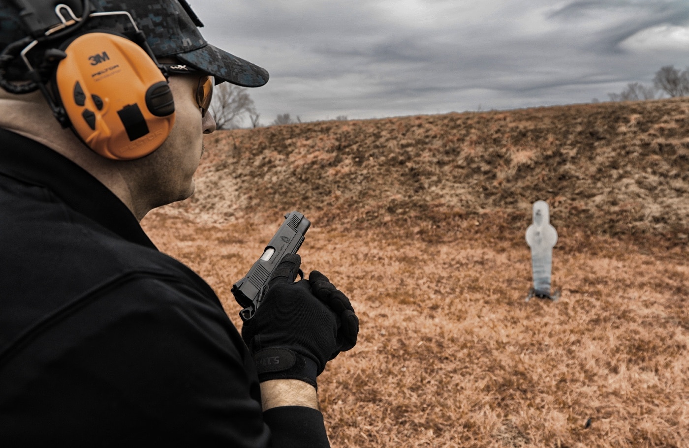 This photograph captures a senior citizen at the shooting range, using gloves to learn how to manipulate handgun controls and soften recoil. The gloves provide a comfortable pad that enhances grip safety and trigger control during target shooting. The image highlights the importance of proper training, safe action, and resilience in defensive shooting skills. It demonstrates how adaptive techniques help overcome challenges such as arthritis and reduced motor skills. The shooter is engaged in shooting sports and active shooter training, ensuring he remains precise and confident with his pistol.