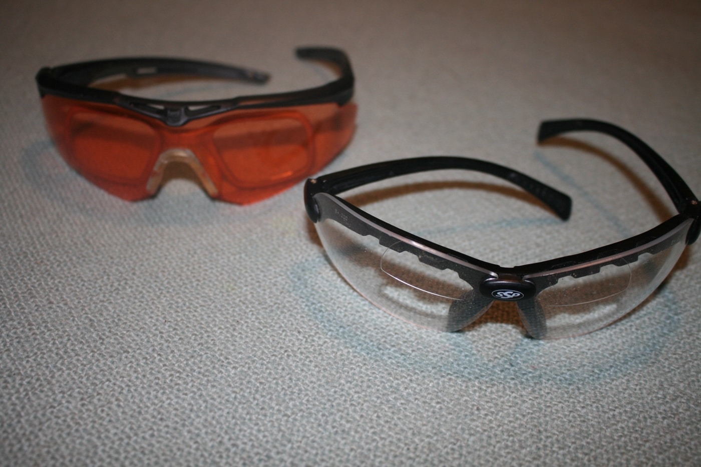 This photograph features several pairs of standard shooting glasses that are essential for shooting sports and target shooting at the firing range. The image is aimed at senior citizens and older adults who value precision when using a handgun or pistol for self defense. It highlights the importance of proper training, safe action, and resilience in maintaining shooting skills despite challenges like arthritis and reduced motor skills. The glasses serve as a tool for improving accuracy, trigger control, and overall performance during active shooter training and home defense scenarios.